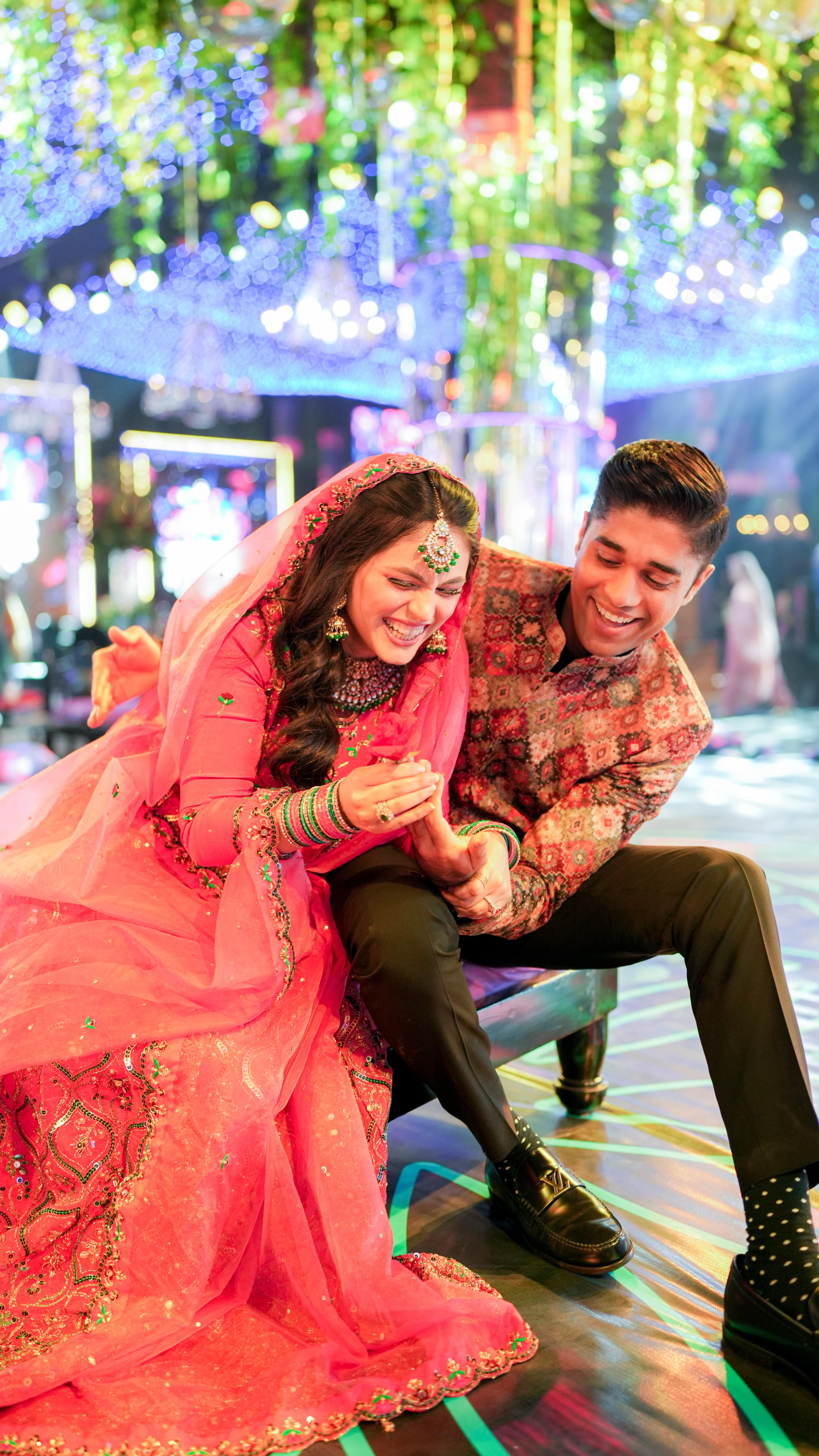 Bride and groom seated together laughing under colourful hanging lights