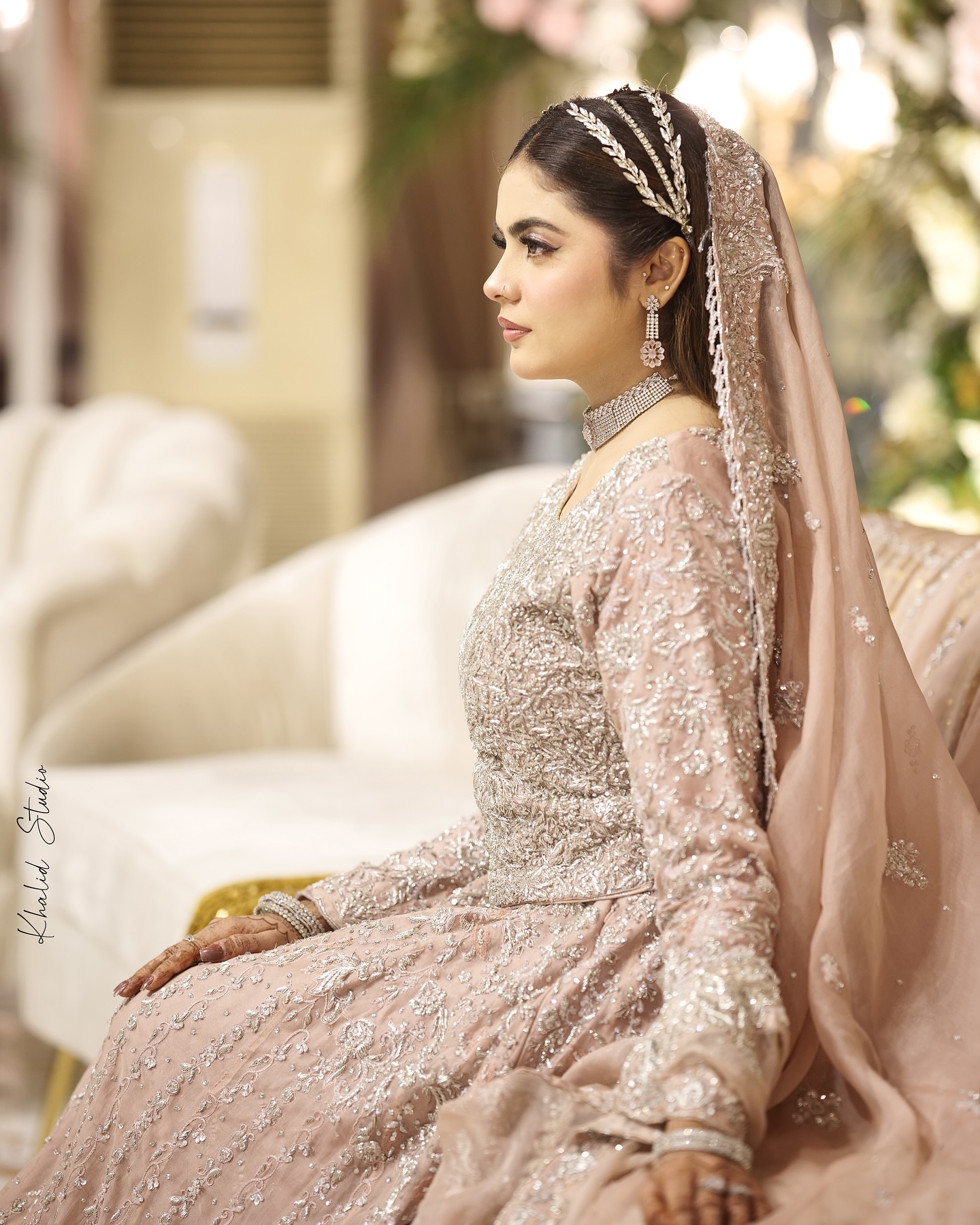 Bride in a red embroidered outfit with henna hands and a gold and emerald choker