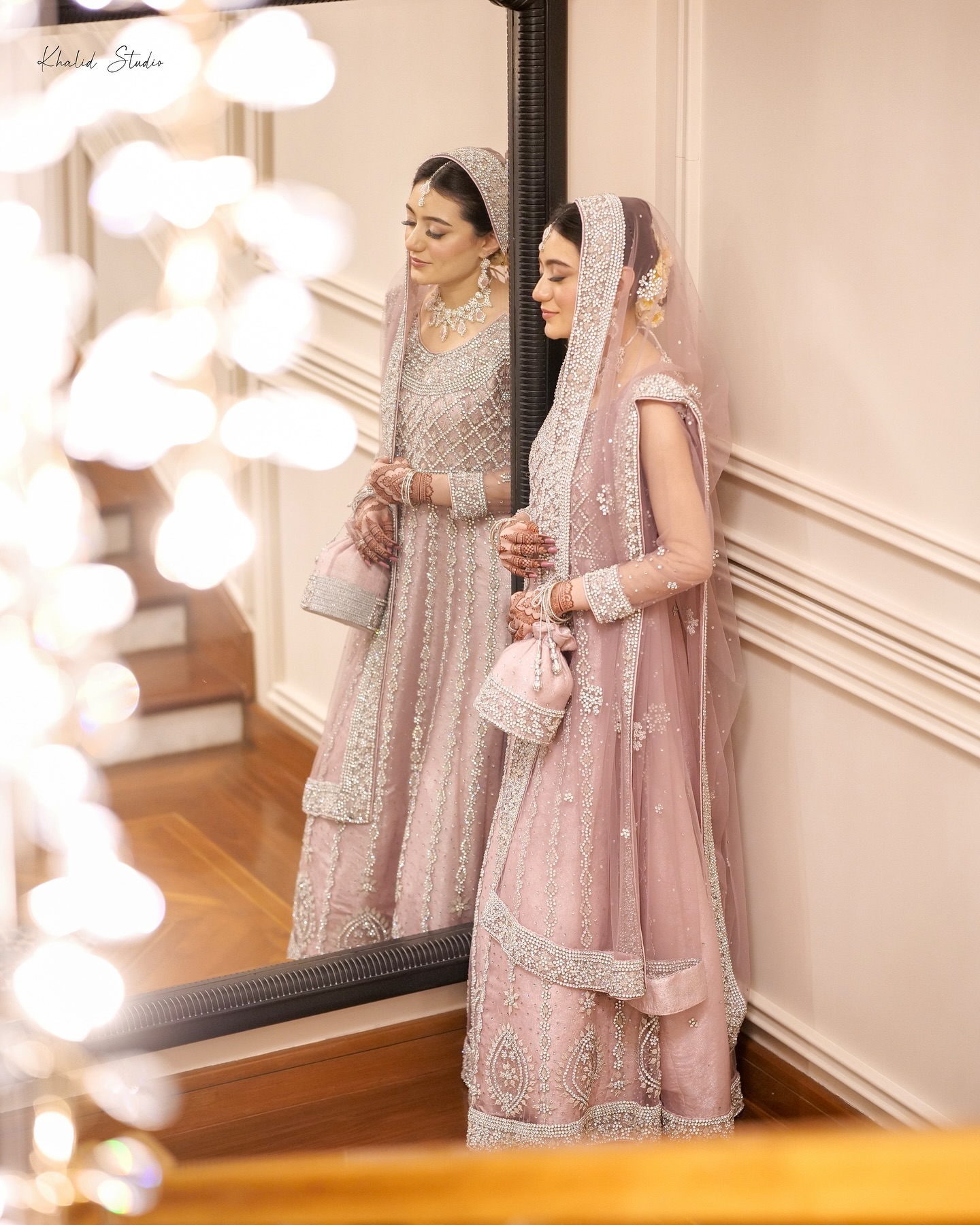 Bride in a maroon lehenga standing beneath hanging pendant lights