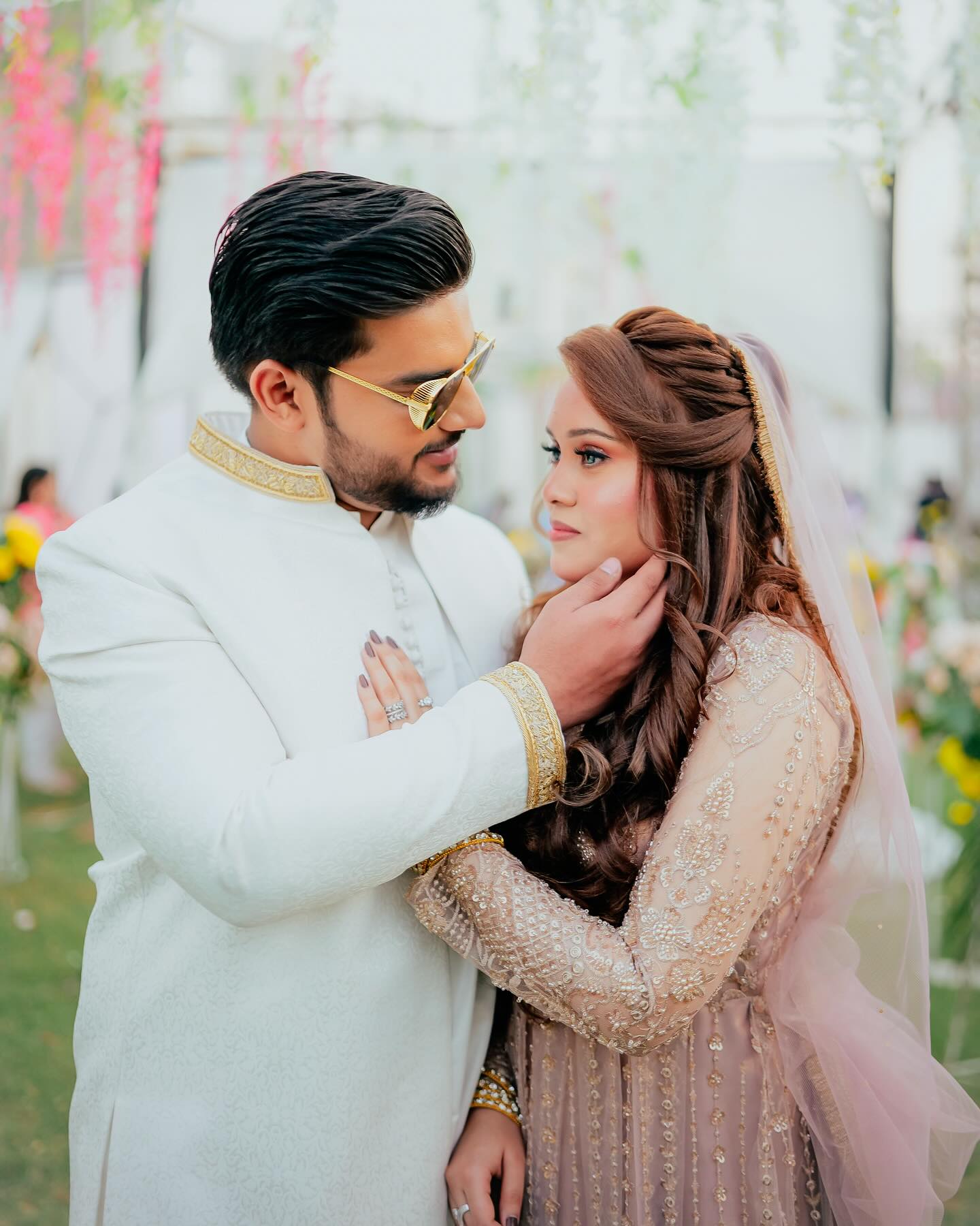 Bride and groom together in a garden, the groom in a white sherwani and gold sunglasses